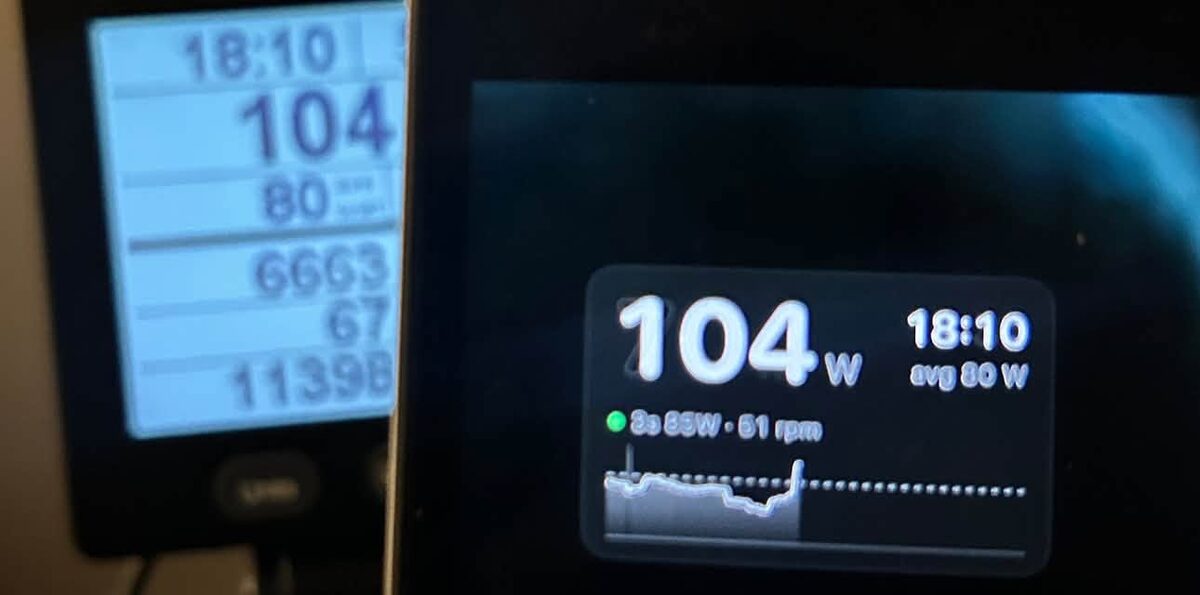 A PM5 monitor showing 104 watts and 18:10 beside a laptop playing a video, with the PowerView window in the corner also showing 104 W, 18:10 and an 80 W average.